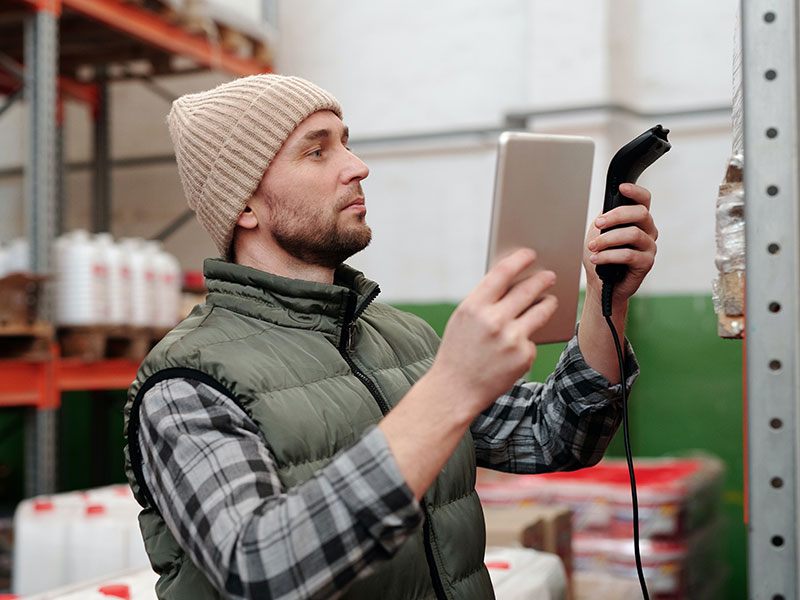 Operatore di magazzino con tablet e lettore barcode davanti a una scaffalatura
